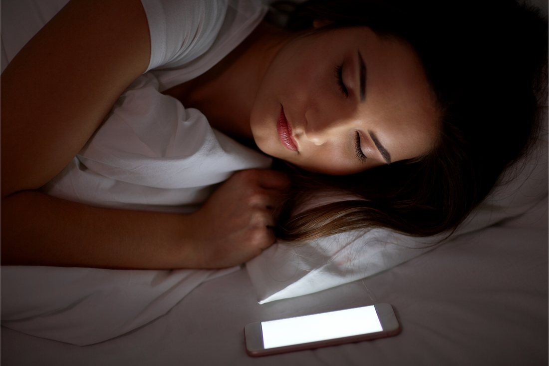 Donna dorme con smartphone acceso vicino che emette luce blu